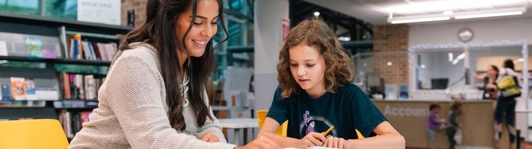 Teenager helping child read at table